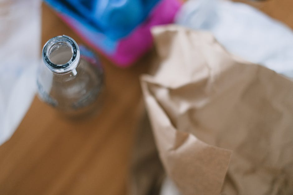 A white plastic bin with a hinged lid, labeled 'PAPER' with bold black letters, is positioned on the floor in a domestic setting, likely a kitchen or utility room. The bin is rectangular with a smooth